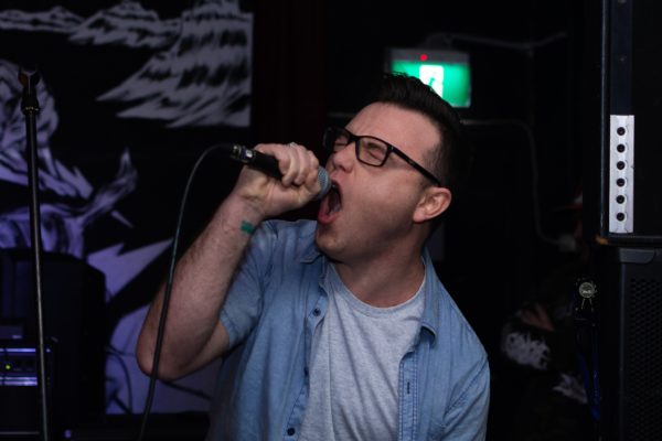 james-dominko-yoMLPhBZwjE-unsplash Junger Mann mit Brille, der Karaoke singt